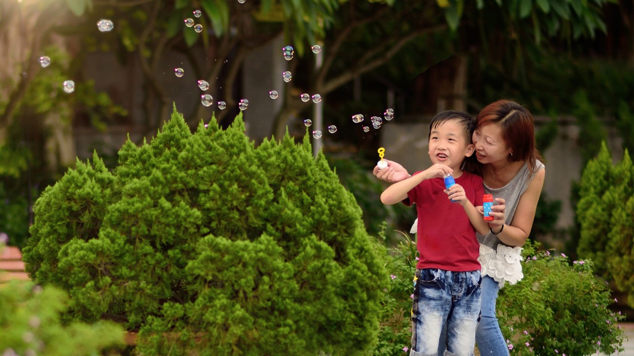 A kid and his mother are playing with bubbles; image used for HSBC Malaysia build emergency savings article page.