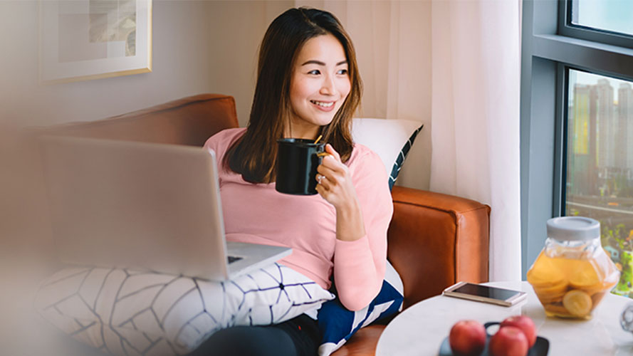A women is using laptop and drinking coffee in the living room; image used for HSBC Malaysia Auto Balance Conversion page.