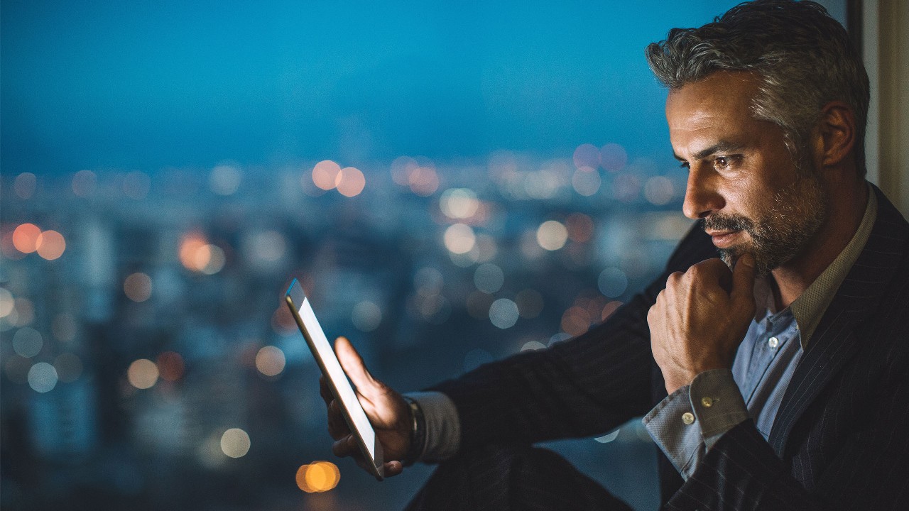 Man looking at his phone at dusk with the city lights behind him. Image used for HSBC Malaysia foreign exchange page.