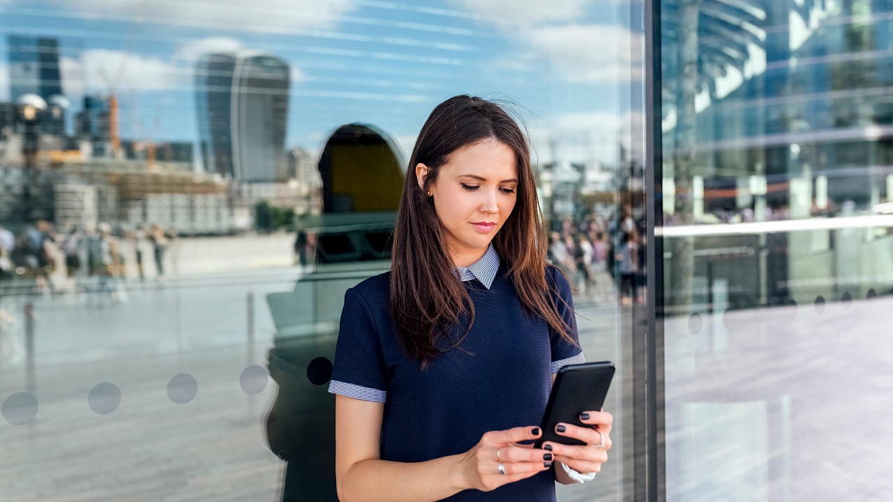 Lady standing outside, leaning against a window while looking at her phone. Image used for HSBC Malaysia DuitNow page.