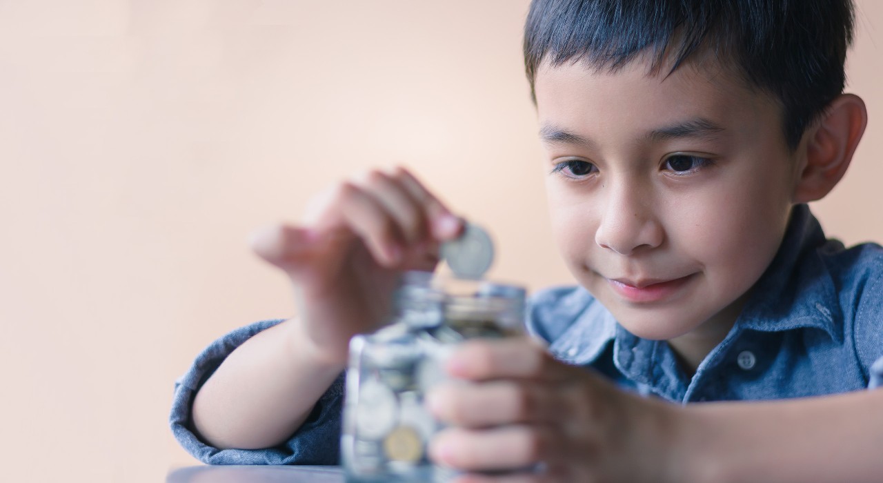 Boy putting a coin into piggy bank; image used for HSBC Malaysia's Teaching kids the 1, 2, 3s of money article page.