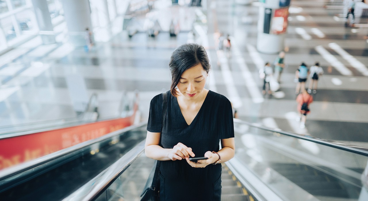 A woman is using her mobile on the escalator; image used for HSBC Malaysia Stay Calm, Invest Smart article